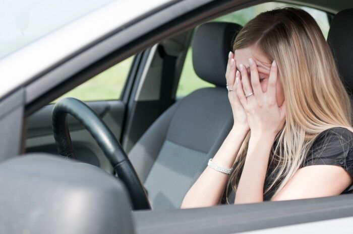 Young woman with hands on eyes sitting depressed in car