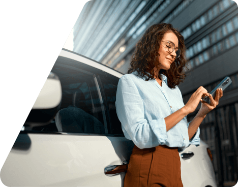 Mujer mirando el móvil apoyada en el lateral de un coche